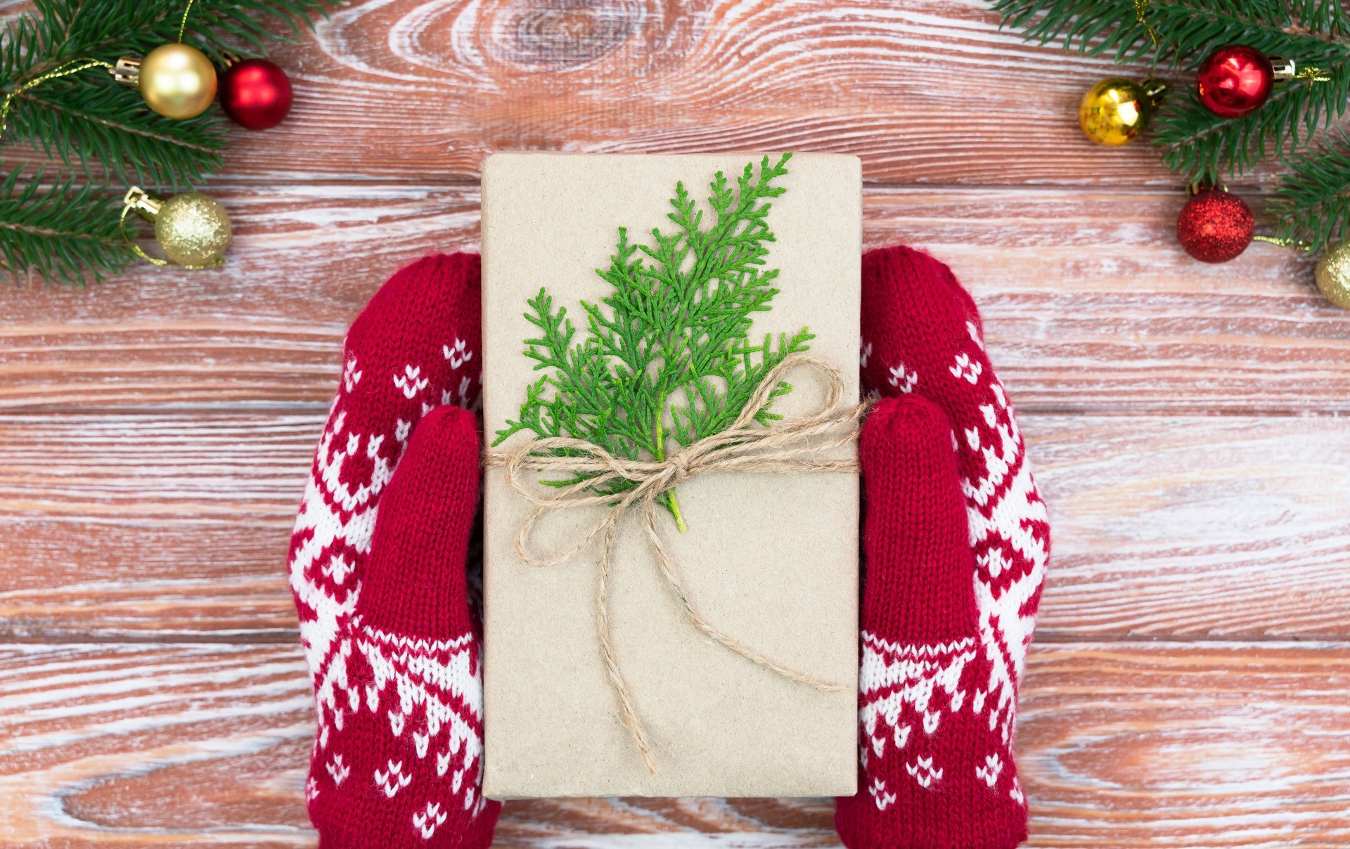 Concept of gift shopping for Christmas and New Year. Woman's hands in winter red gloves hold christmas gift on a wooden background. Top view. Close-up.