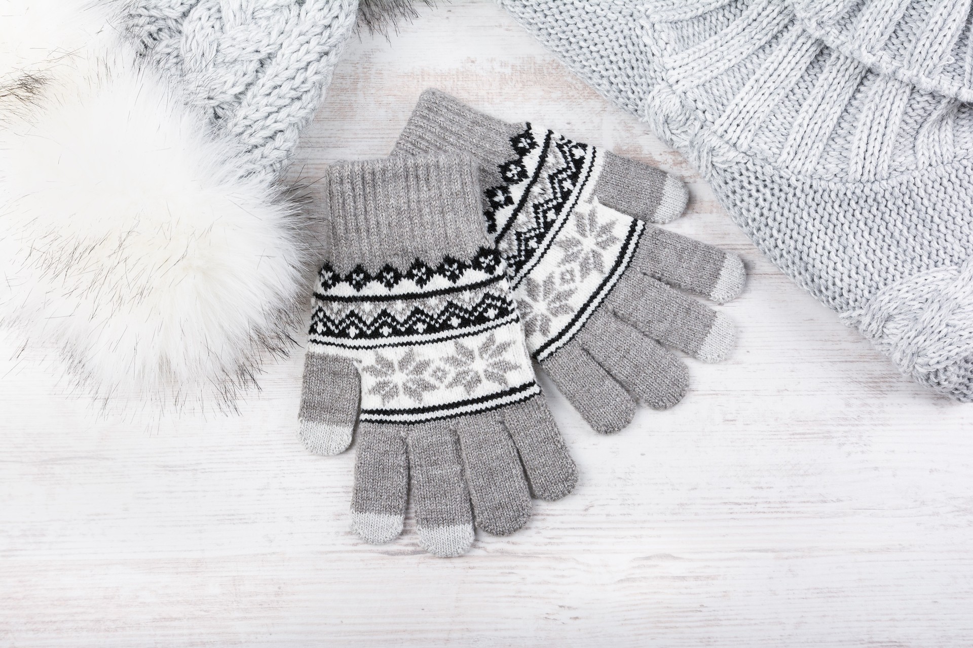 Winter knitted gloves, fur hat and pullover on white wooden background. Set of grey knitted clothes.
