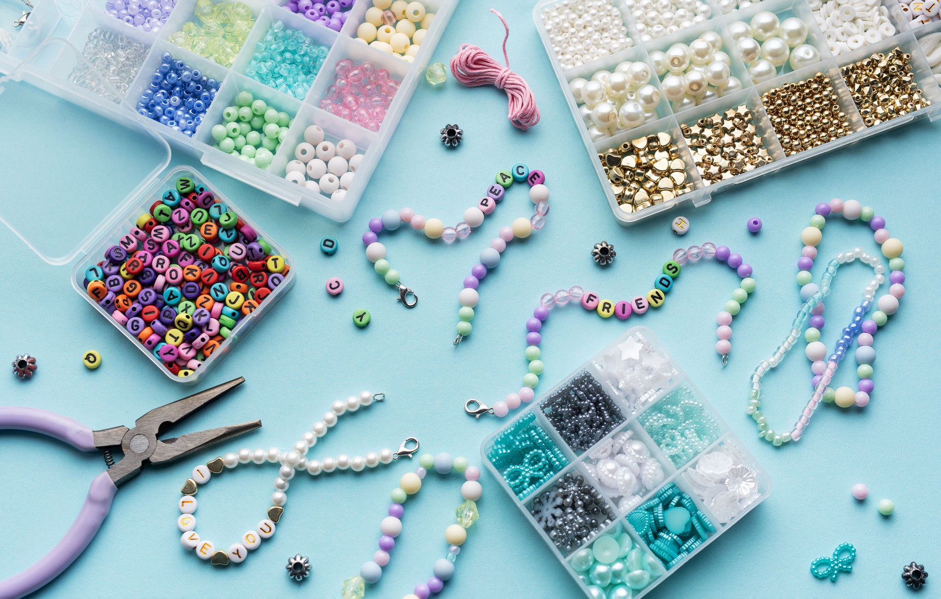 Colorful assortment of beads and jewelry-making tools on a blue surface with completed bracelets
